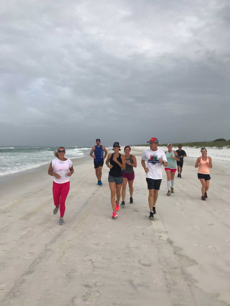 A small group of adults smiling while running on the beach